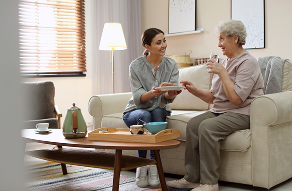 young woman serving food to elderly woman in cozy living room enjoying quality time together while sharing 9 memorable moments