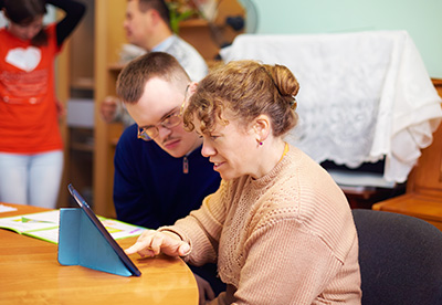 woman and man engaged in conversation while using digital tablet in classroom with others in background learning environment 2 people 2 tablets