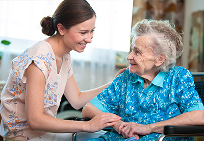 a caregiver smiling and engaging with an elderly woman in a nursing home setting emphasizing companionship for seniors and the importance of care at age 12 and beyond