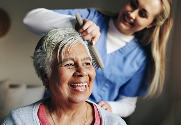 a smiling elderly woman getting her hair combed by a caregiver in a comfortable setting enjoying quality time together 2 hair care moments 2 caregiver support