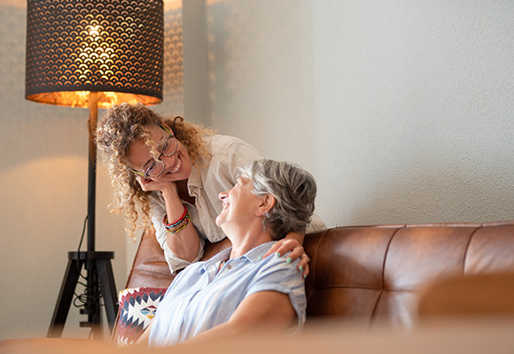two women enjoying a joyful moment together on a couch with a decorative lamp in the background